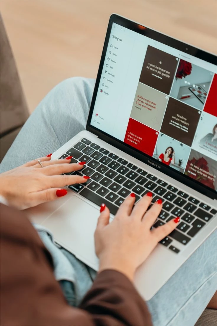 Mãos com unhas vermelhas usando um notebook com um feed do Instagram